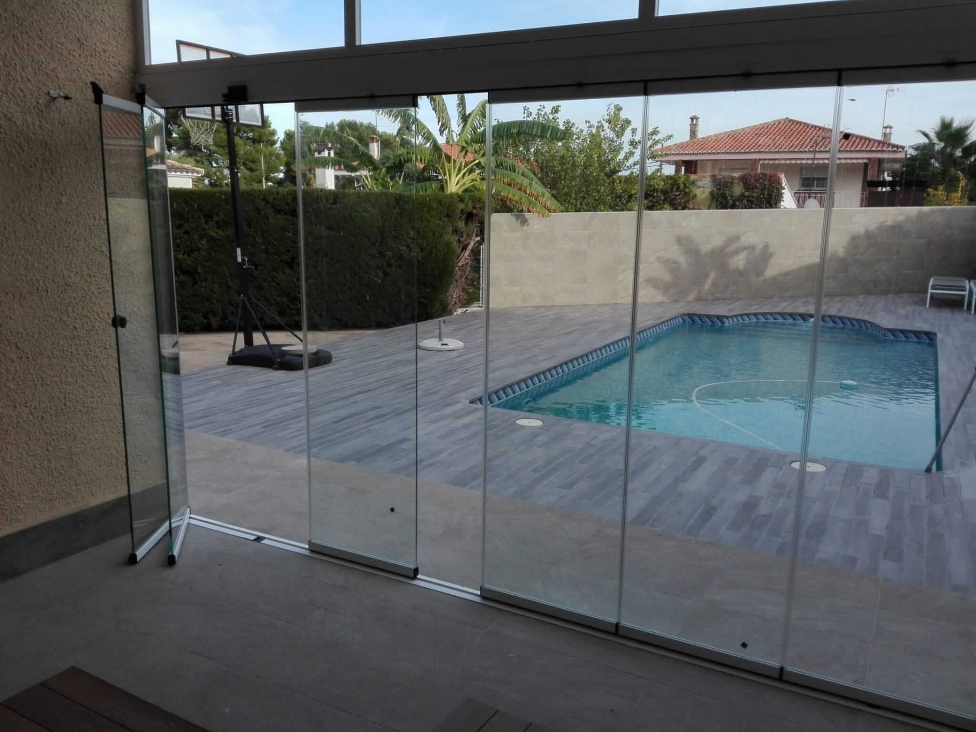 Balconera de cristal transparente de 6 hojas abierta, con piscina de fondo